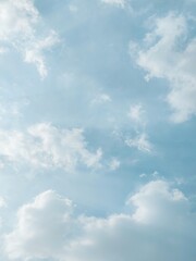 Cumulus clouds drift across a soft pale blue sky illuminated by diffused morning sunlight, creating a calm atmosphere. © choyi