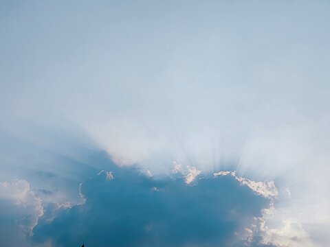 Cloud edges glow with bright sunbeams bursting upward into a pale hazy blue sky during afternoon light.