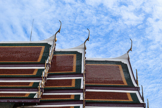 Multi-tiered temple roof of Wat Rakhang in Bangkok, Thailand, showing gold chofa finials and green, maroon, and gold tiles against a blue sky, for Thai Buddhist architecture and tourism content.