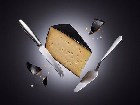 Danbo cheese wedge with black wax rind floating in studio