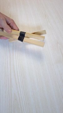 Hands slicing electrical tape from bundled wood, cutting through black tape binding multiple slats with retractable blade, strips peeled to reveal glue marks and stain, efficient