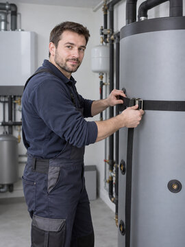 Heating technician tightens securing strap around buffer tank in utility room