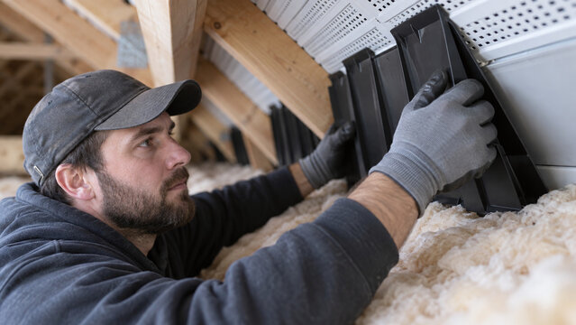 Loft installer carefully pushes ventilation baffles into insulated roof eaves