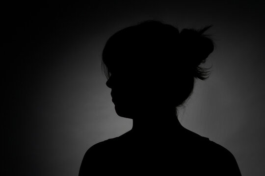 Silhouette portrait of a young teenage girl posing against a dark background