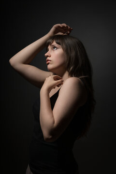 Portrait of a young woman looking up with a thoughtful expression in dark studio setting