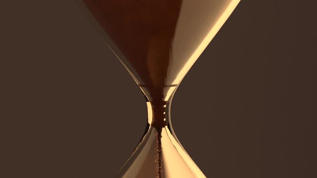 Panning camera showing glass hourglass pouring sand via thin neck in studio, timing, cone forming