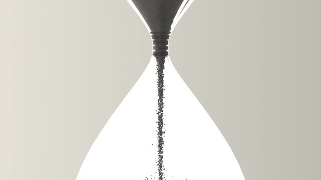 Pouring clear glass hourglass releasing dark sand through neck under gravity in studio