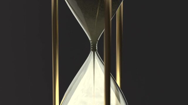Hourglass showing gravity pulling pale sand through neck at studio, forming pile with gold supports