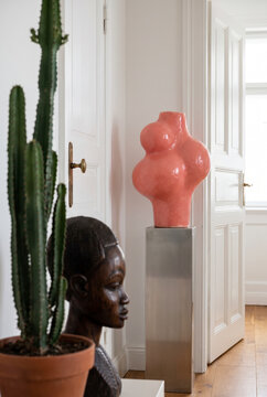 Solitary coral sculpture on a steel pedestal beside a cactus and carved wooden bust