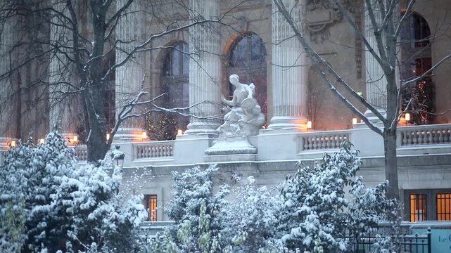 Close-up view of the snow-covered statue and neoclassical facade of the Grand Palais in Paris. Snow falls gently on the surrounding trees and architecture
