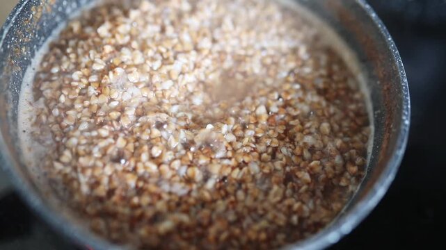 Buckwheat groats boiling and bubbling in a small saucepan on a kitchen stove during home cooking