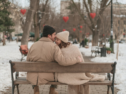 Happy Romantic Couple Sitting on a Bench in Winter Park Hugging and Enjoying Time Together