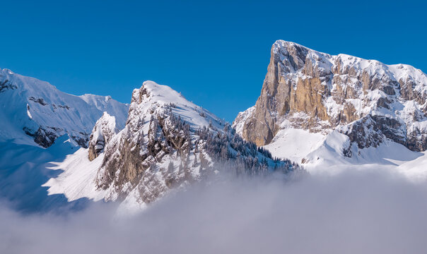 Aerial view of Pic de Bure and Crete d&rsquo;Ane in the Devoluy Massif, with snow-covered limestone cliffs emerging through mist in the French Alps. Hautes-Alpes, France