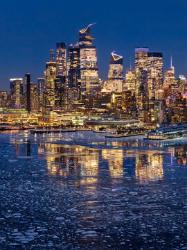 Aerial winter view of Manhattan skyline with Hudson Yards skyscrapers illuminated at twilight. Frozen Hudson River with floating ice. New York City
