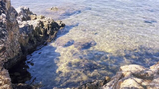 Sunlight shimmering across crystal clear shallow cove water revealing submerged rocks and moss on the Ayvalik, Ortunc Bay.