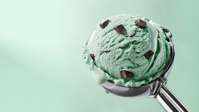 Scoop of mint chocolate chip ice cream in a metal scooper on a soft green background, dessert and frozen treat concept with wide copy space for text