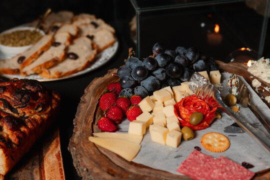 A platter of cheeses, fruits, and cured meats arranged on a rustic wooden base.