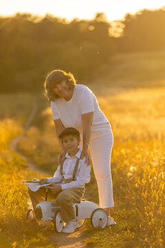 Sweet preteen child, boy, playing in a field on sunset with kite and old vingate car, walking with grandmother in the countryside