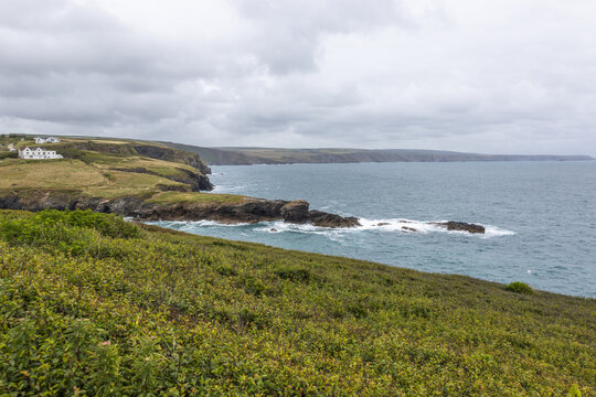 View over coastal headland with waves crashing on rocky cliffs and grassy hills