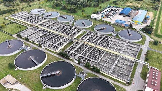 Aerial view of sewage treatment facilities showcasing multiple circular tanks and rectangular filtration systems in a green urban landscape with water channels and surrounding vegetation. Ecology conc