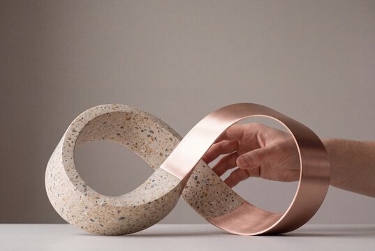 A male hand reaches through an infinity loop sculpture made of composite terrazzo and brushed copper metal in a studio setting