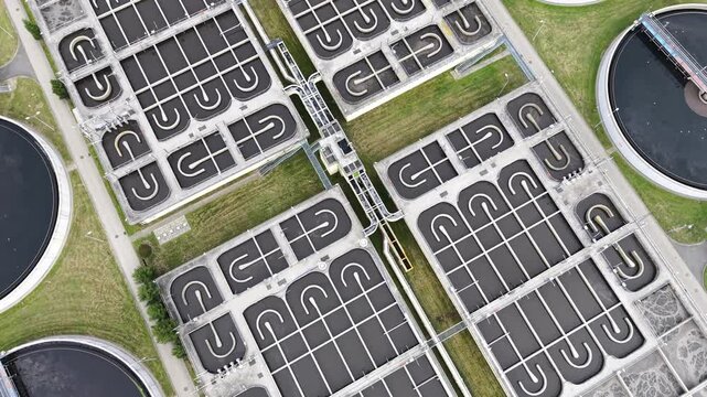 Aerial view of sewage treatment facilities showcasing multiple circular tanks and rectangular filtration systems in a green urban landscape with water channels and surrounding vegetation. Ecology conc