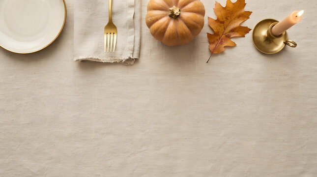 Thanksgiving table setting with pumpkin, autumn leaf, and candle on a linen tablecloth with copy space