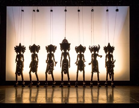 Five traditional Southeast Asian puppet silhouettes with ornate crowns backlit against white background. Cultural heritage performance art, dramatic lighting, traditional costumes.
