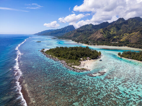 Aerial view of Mo'orea island featuring lush tropical vegetation, white sand beaches, and vibrant turquoise coral reefs in the lagoon, Moorea-Maiao, Windward Islands, French Polynesia.