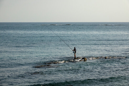A lone fisherman casts his line from a rocky outcrop into the calm sea, South Governorate, Tyre, Lebanon