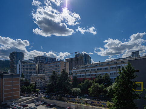 A commercial stock photograph of an urban city view featuring a mix of residential high-rises, commercial buildings, a construction crane, and parked cars, all set beneath a vibrant blue sky filled