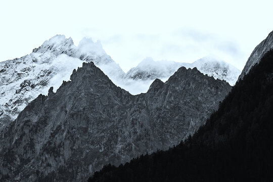 Aerial view of Valchiavenna mountains with snow-capped peaks, rocky ridges, and clouds in Lombardy, Italy.