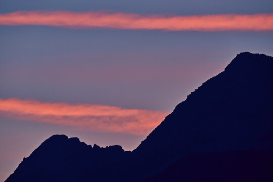 Aerial view of the silhouette of the Valchiavenna mountains against a vibrant sunset sky with pink clouds in Lombardy, Italy.