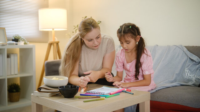 Woman and young girl drawing and coloring together at home.