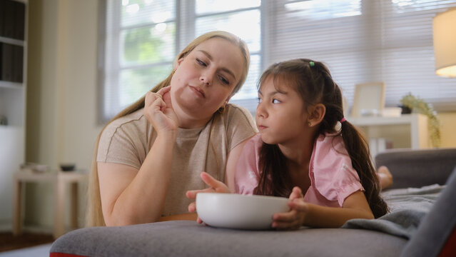 Woman and young girl sharing snacks while relaxing together on a sofa.
