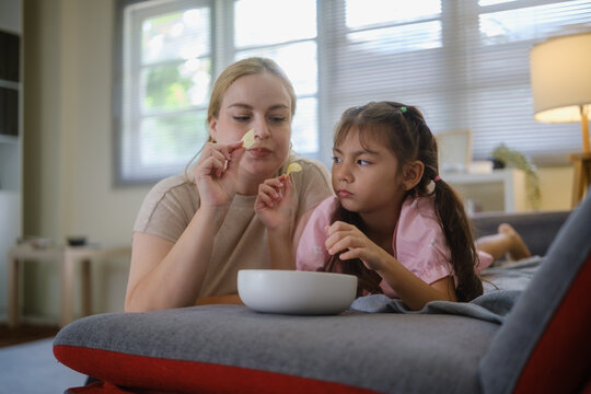 Woman and young girl sharing snacks while relaxing together on a sofa.
