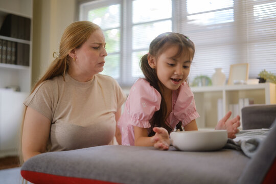 Woman and young girl sharing snacks while relaxing together on a sofa.