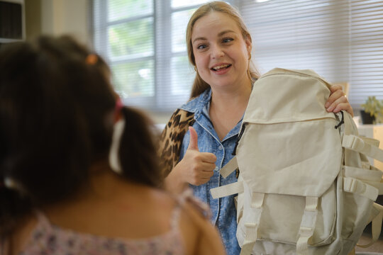 Woman helping a young girl pack and prepare a backpack at home.