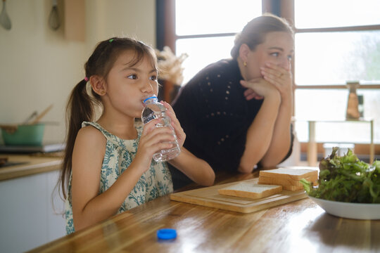 Woman caring for a young girl with throat discomfort in the kitchen.