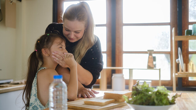 Woman caring for a young girl with throat discomfort in the kitchen.