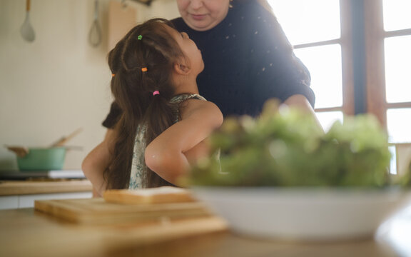 Woman caring for a young girl with throat discomfort in the kitchen.