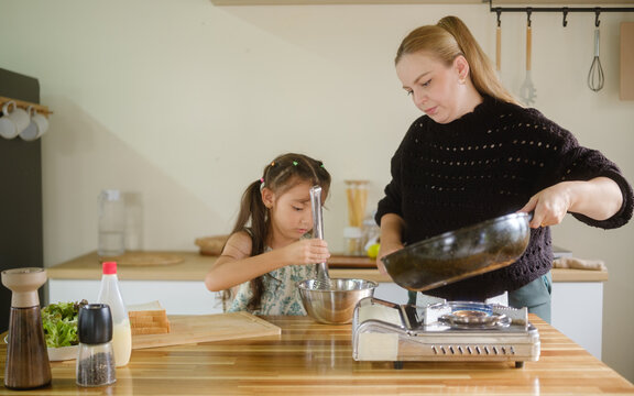 Woman and young girl preparing a meal together in a home kitchen.