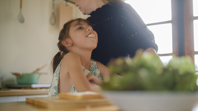 Woman caring for a young girl with throat discomfort in the kitchen.
