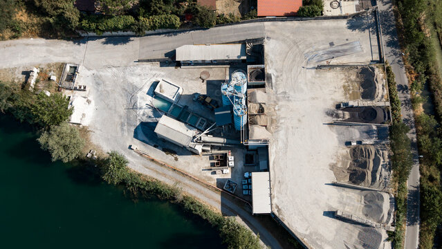 Aerial view of a cement plant with storage silos, gravel piles, and industrial facilities located near a lake in Milan, Lombardy, Italy.