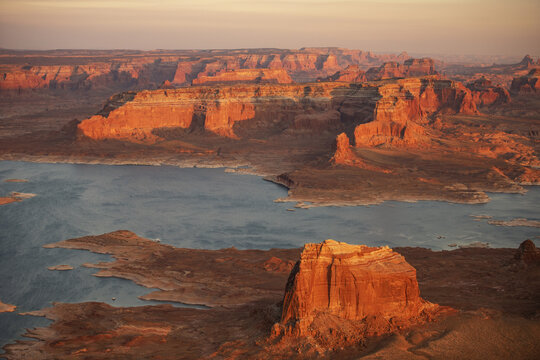 Aerial view of Lake Powell at sunset, showcasing the red sandstone cliffs, calm blue water, and rugged desert landscape in Page, Arizona, United States.