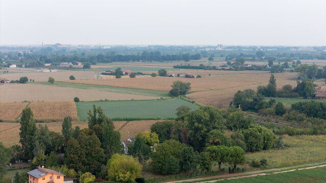 Aerial view of agricultural fields, including tomato crops, surrounded by trees and rural houses in the countryside in Castelvetro Piacentino, Emilia-Romagna, Italy.