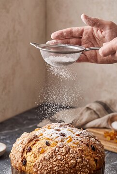 Baker Dusting Traditional Italian Panettone Christmas Cake with Powdered Sugar Using Sieve