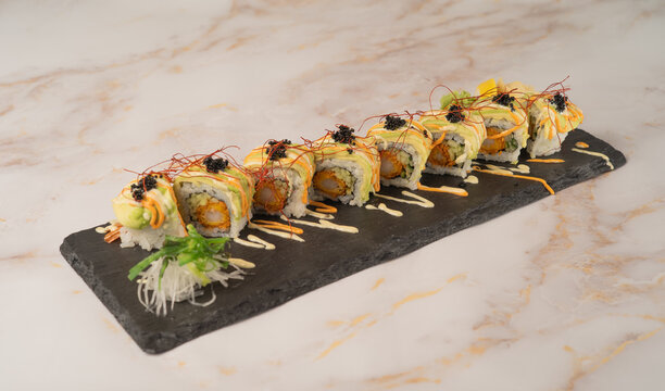 Fancy ebi tempura sushi rolls topped with sliced avocado, black caviar, and chili threads on a black slate platter