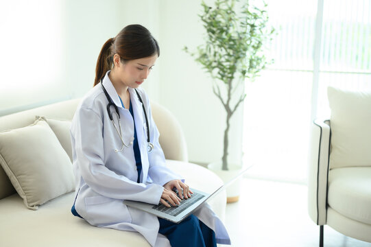 A female doctor is sitting and working at the clinic while waiting to examine patients.