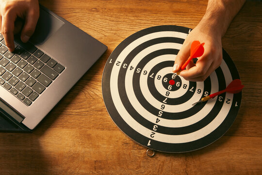 Man's hand is aiming at the target with red dart arrow.